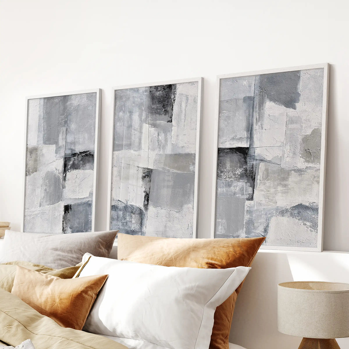 A three-piece print set of gray abstract textures rests in white frames above the bedroom bed, adding a soothing neutral accent with gentle depth.
