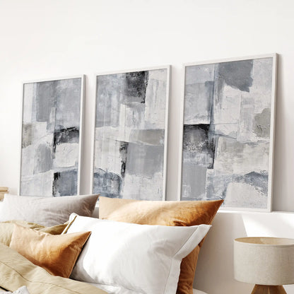 A three-piece print set of gray abstract textures rests in white frames above the bedroom bed, adding a soothing neutral accent with gentle depth.
