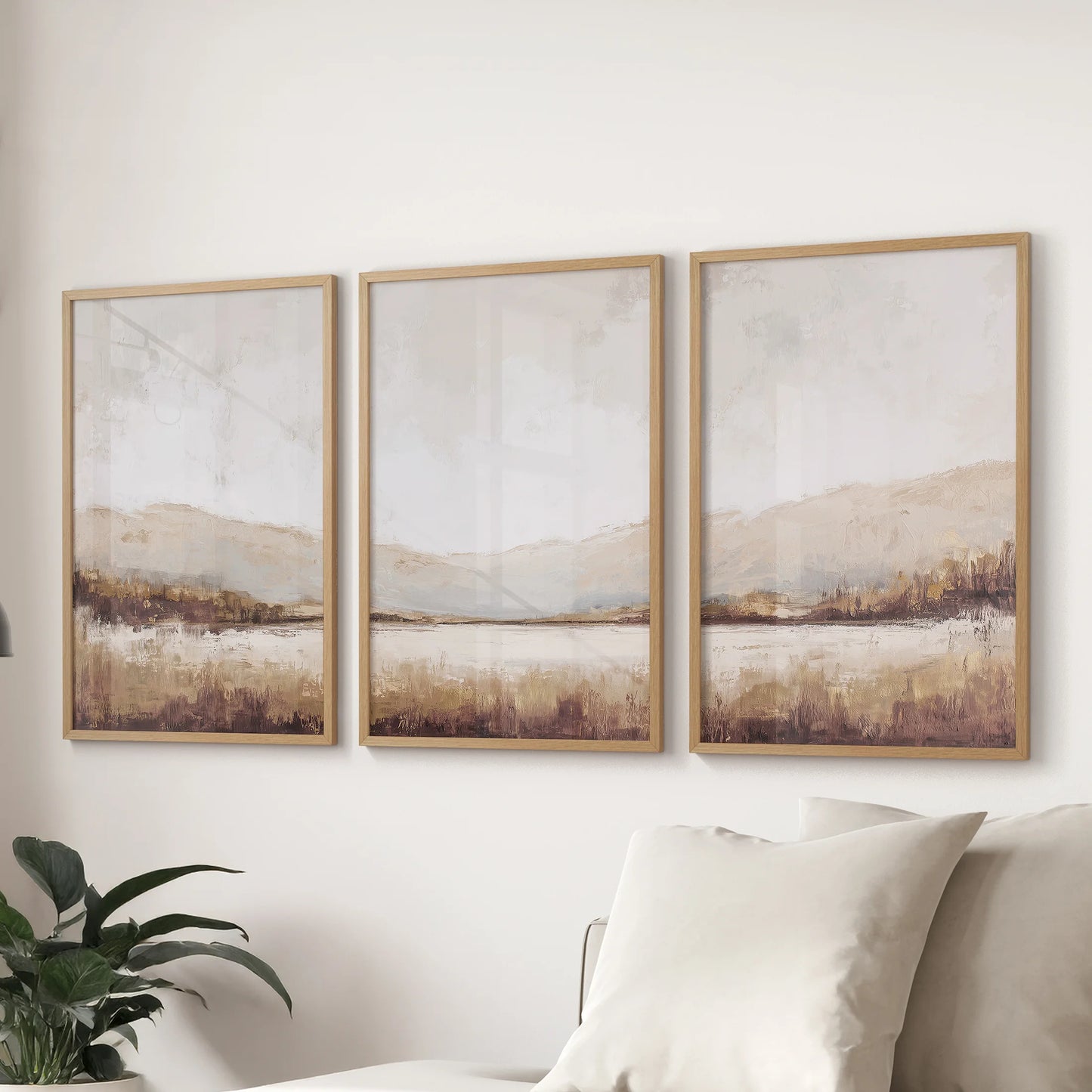 Beige and brown landscape print set of three in wooden frames hangs above the living room couch, lending minimal warmth and quiet balance.