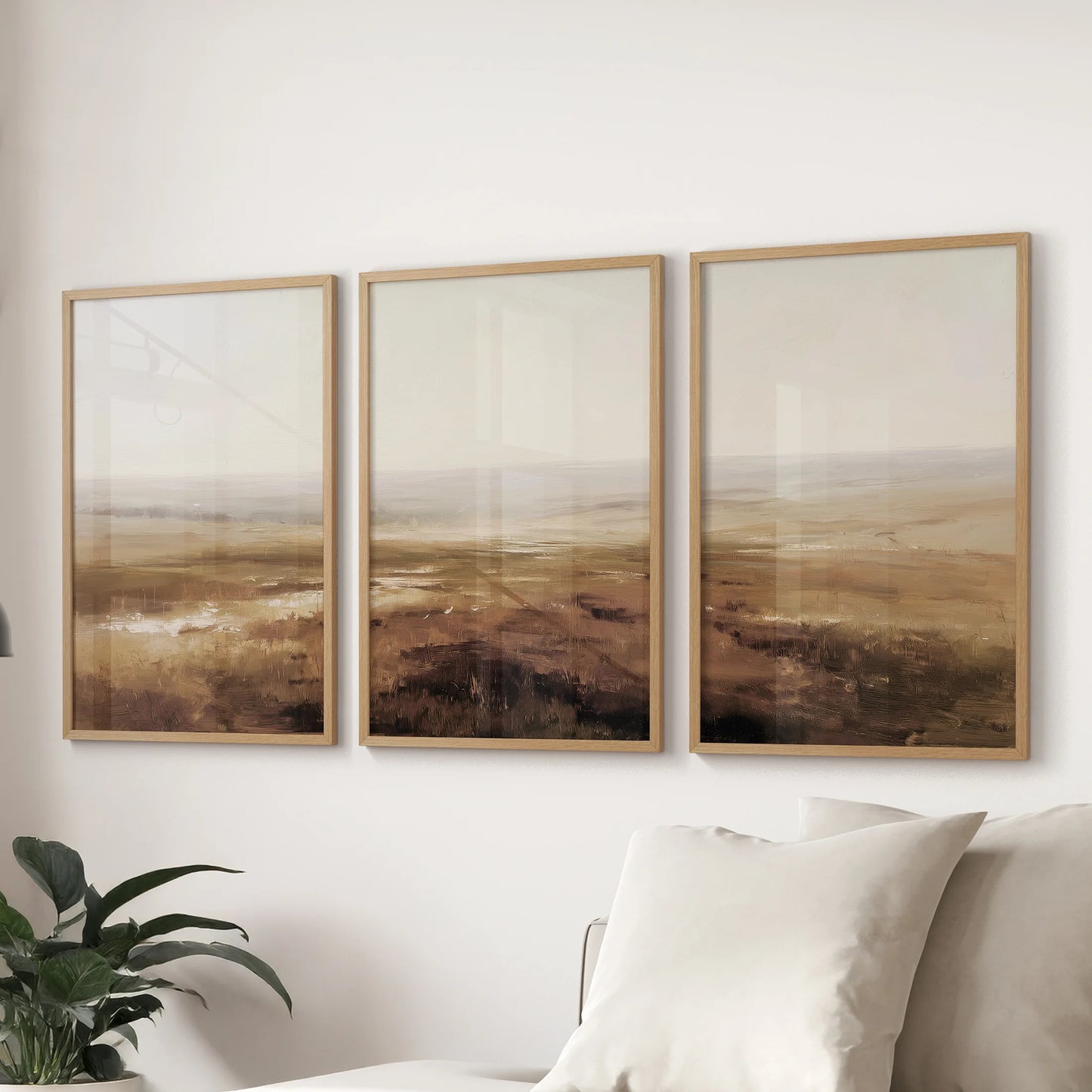 Moody neutral landscapes as three framed prints create subtle wall art behind the sofa in a family room, shown in thin wood frames.