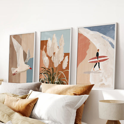 Three white-framed art prints of pampas grass by the dunes hang above the bed, lending gentle texture and a tranquil beach feel to the bedroom.