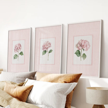 Pastel botanical flowers in a three-piece wall picture set are white framed and arranged above the bed headboard in a bedroom.
