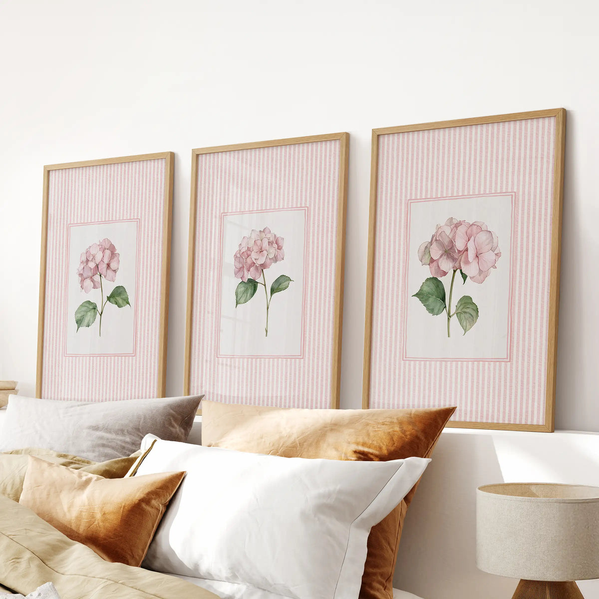 Wall art trio of pastel botanical flowers in oak frames over a bedroom headboard.