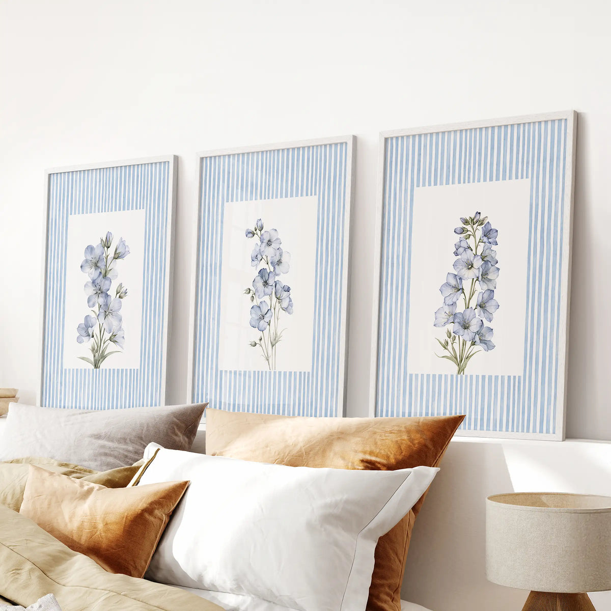 Pastel botanicals three-piece wall art set in white frames, displayed over the headboard in a bedroom with light blue walls and striped bedding.