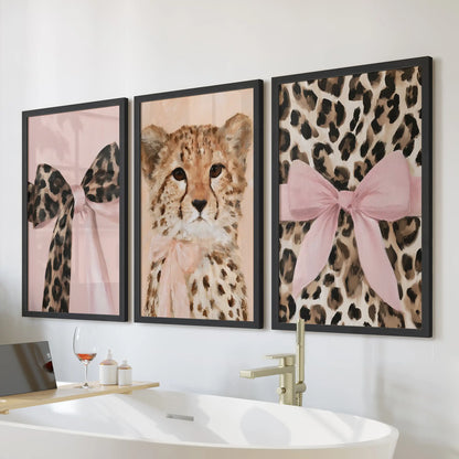 Three wall art prints of pink-bow leopard portraits sit in sleek black frames over the bathtub, adding a chic touch to the bathroom.