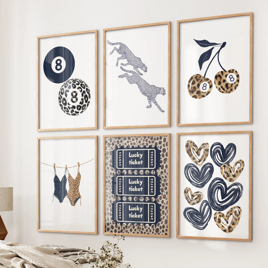 Six cheetah print art prints in natural wood frames form a warm little gallery on a bedroom wall, mixing navy hues with a soft coquette touch.
