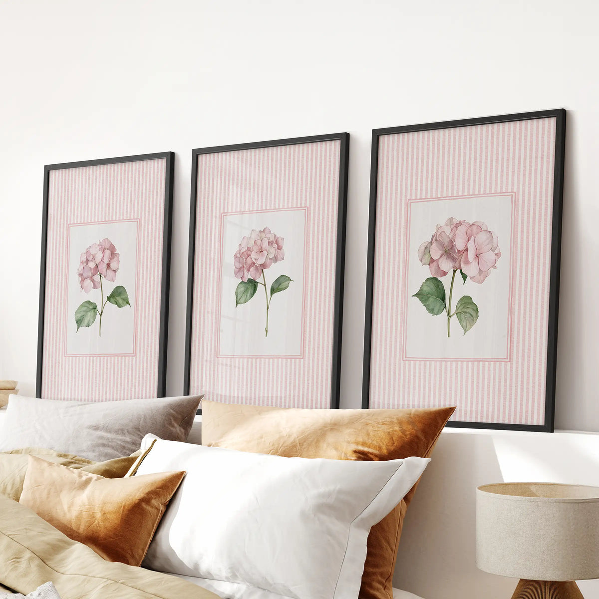 Blush pink flowers in a wall hanging set of 3 are arranged in black frames over the headboard in a bedroom.