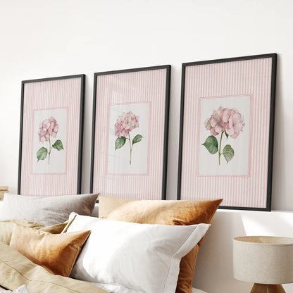 Blush pink flowers in a wall hanging set of 3 are arranged in black frames over the headboard in a bedroom.