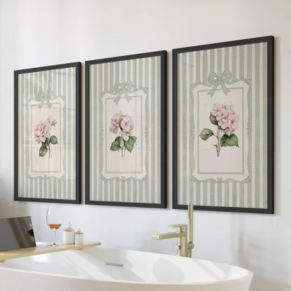 Sage green striped botanicals in a set of three wall posters hang above a bathroom bathtub in slim black frames.