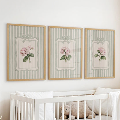 Sage green striped botanicals in a set of three wall hangings are displayed over a nursery bassinet in wood frames.