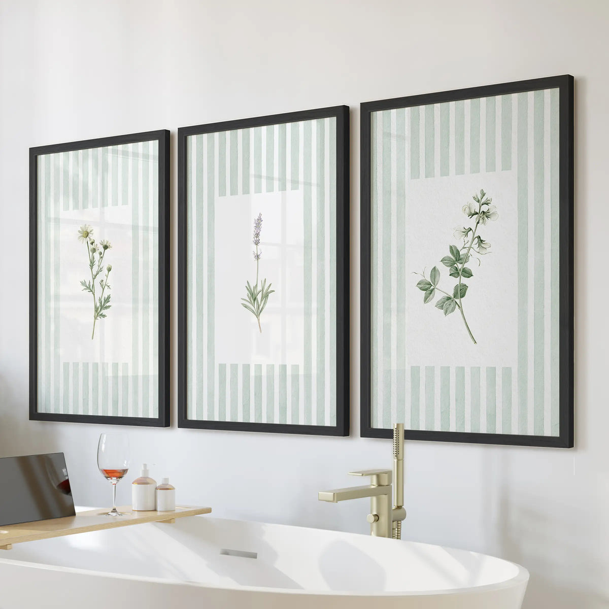 Sage green wildflower wall art in a three-piece set hangs in black frames above a soaking tub in a bathroom with tiled walls and a wood vanity.