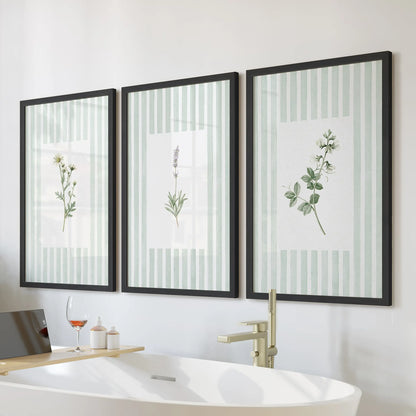 Sage green wildflower wall art in a three-piece set hangs in black frames above a soaking tub in a bathroom with tiled walls and a wood vanity.