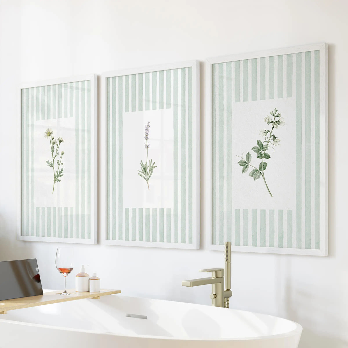 A set of three sage green wildflower wall art prints in white frames hangs over a bathtub in a bathroom.