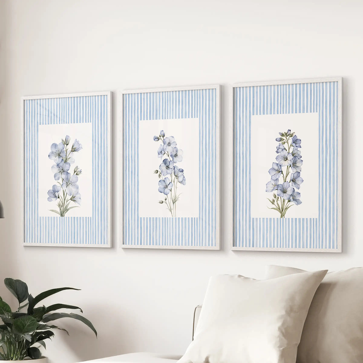 Three-print gallery wall of striped botanical florals in white frames, arranged above a sectional sofa in a light blue lounge.