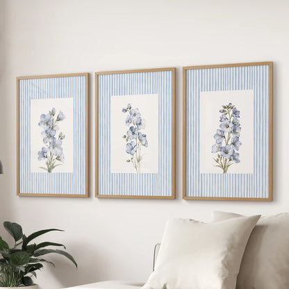 Three-piece wall art set of striped botanical florals in thin wood frames, arranged above a pale sofa in a light blue living room.