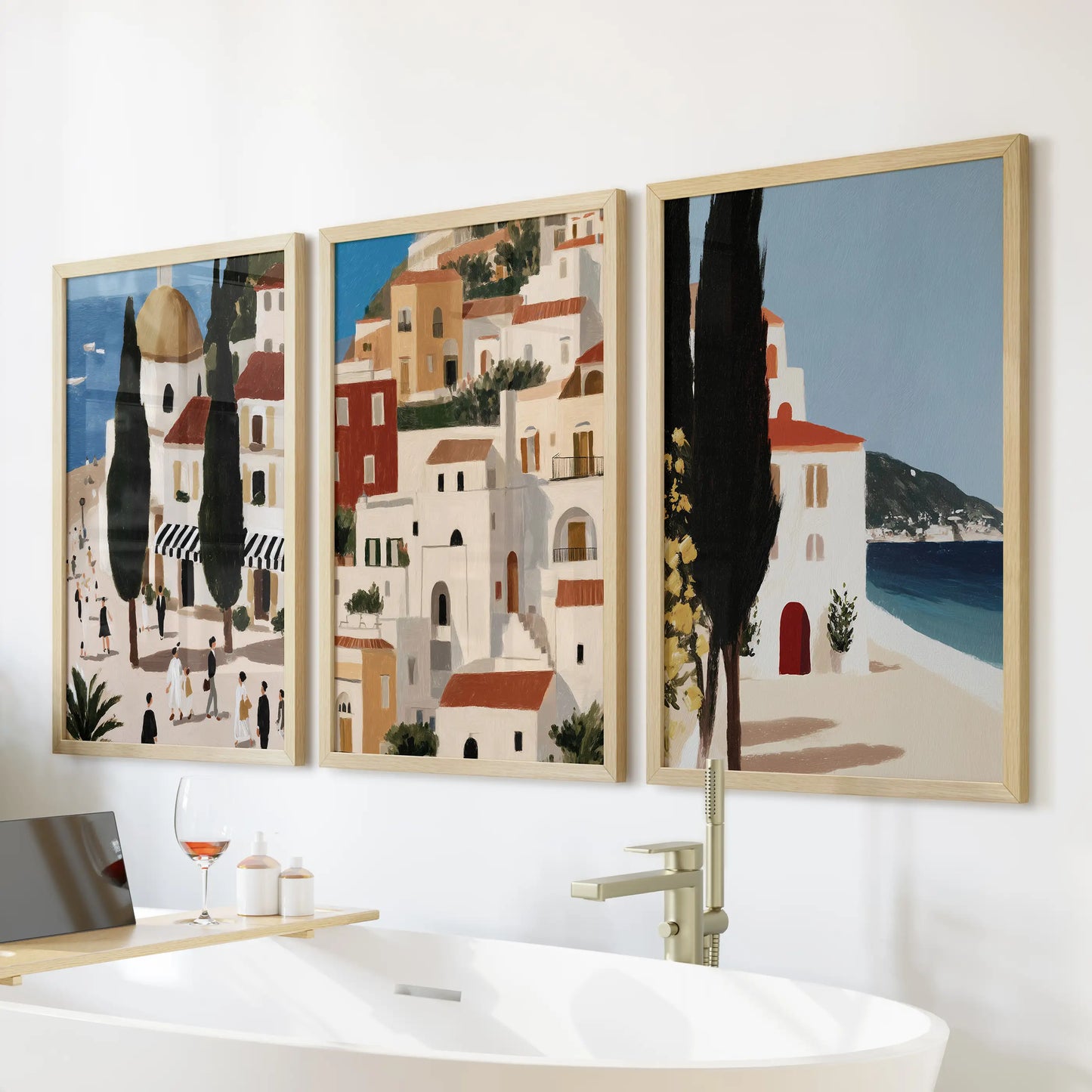Three vintage Mediterranean art prints in warm wood frames sit above the freestanding tub, softening the bathroom with gentle coastal warmth.