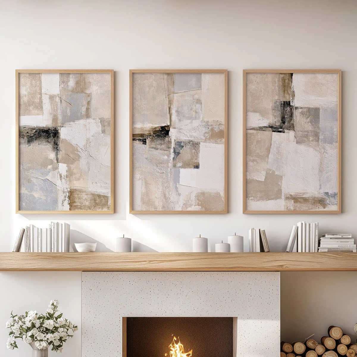 Three framed abstract canvas prints in a light wood frame are displayed side-by-side on a white wall above a fireplace mantel decorated with books, candles, and a small vase of flowers.