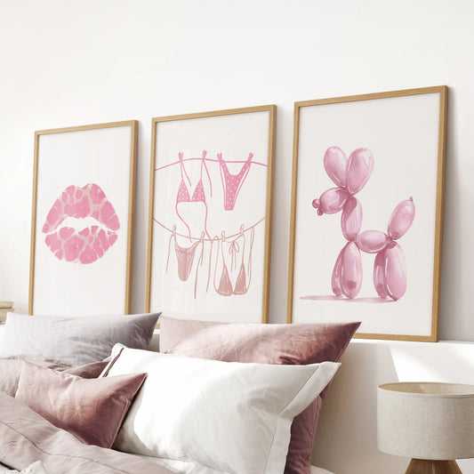 A gallery wall set of 3 oak-framed prints lips, bikini, and balloon dog completes the pink bedroom with balanced styling above the headboard.