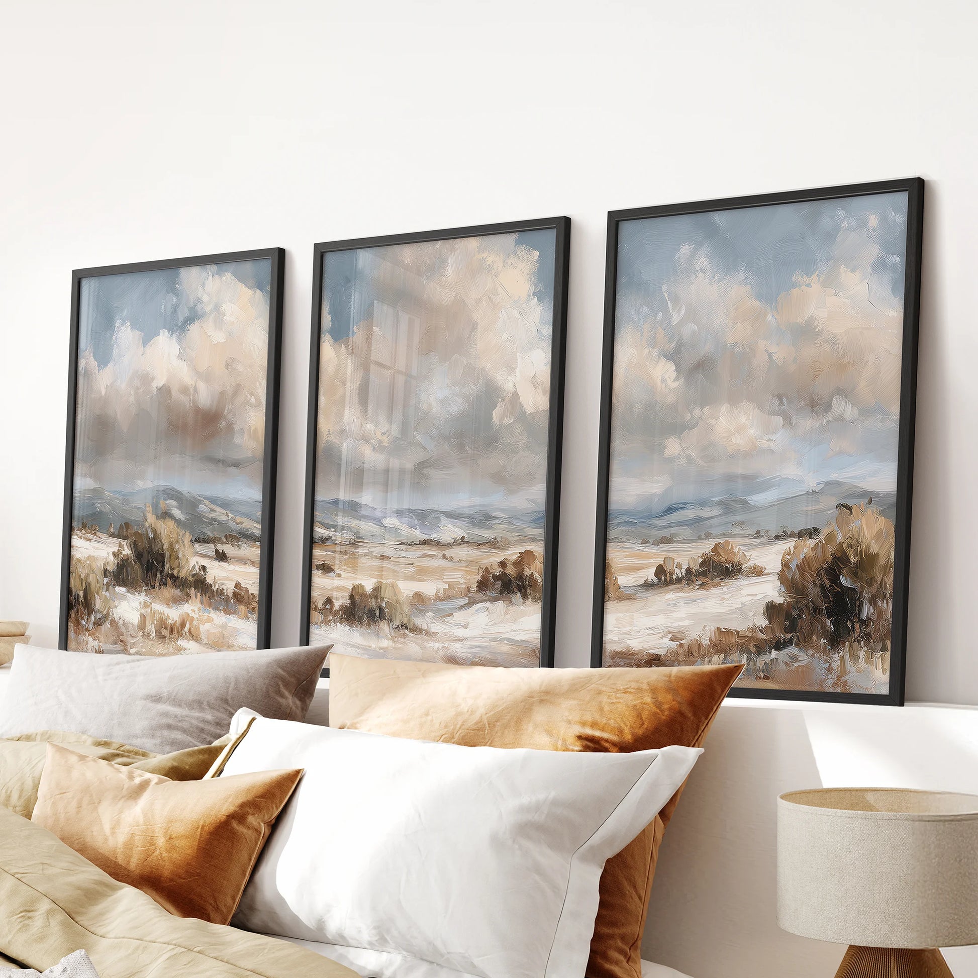 Neutral landscape prints, set of three, in black frames bring soft beige, brown, and blue wall art to a bedroom, styled as a calm row above the bed.