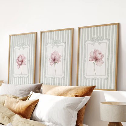 Set of three floral wall art prints in thin wood frames, showing pink peonies on sage green stripes over a bedroom headboard.