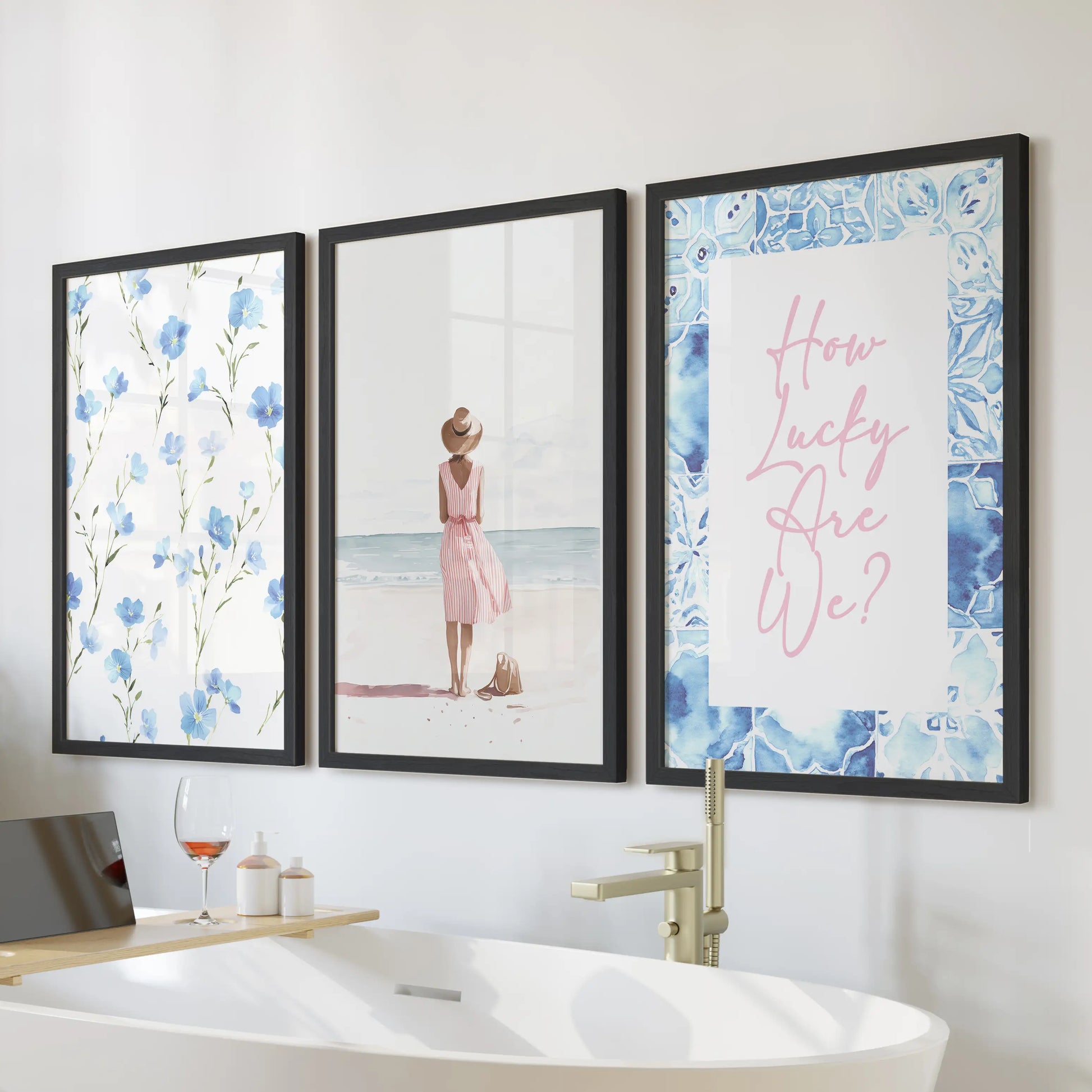A three-piece wall art set of watercolor beach scenes in sleek black frames hangs above a freestanding tub, giving the bathroom a calm seaside feel.