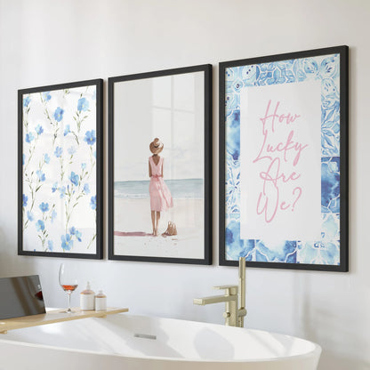 A three-piece wall art set of watercolor beach scenes in sleek black frames hangs above a freestanding tub, giving the bathroom a calm seaside feel.