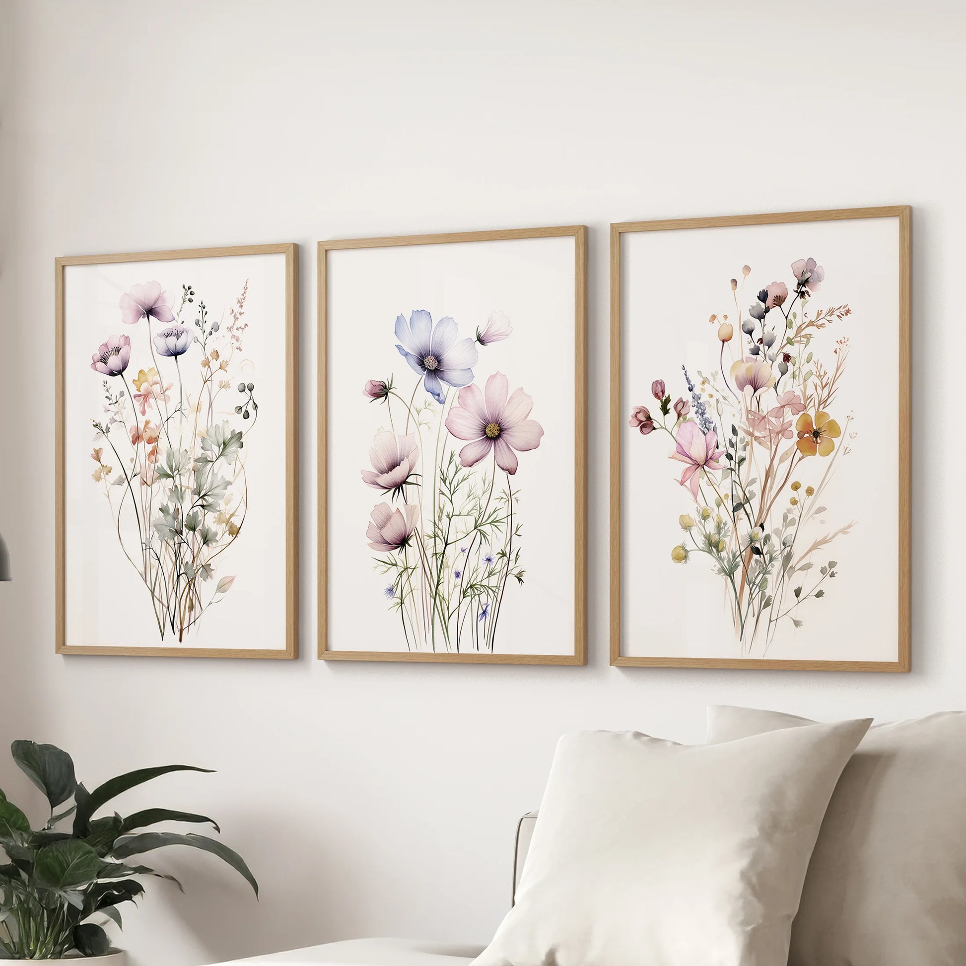 Plant botanical art in a three-print wall set features natural wood frames and spans the living room wall behind the couch with airy wildflower detail.