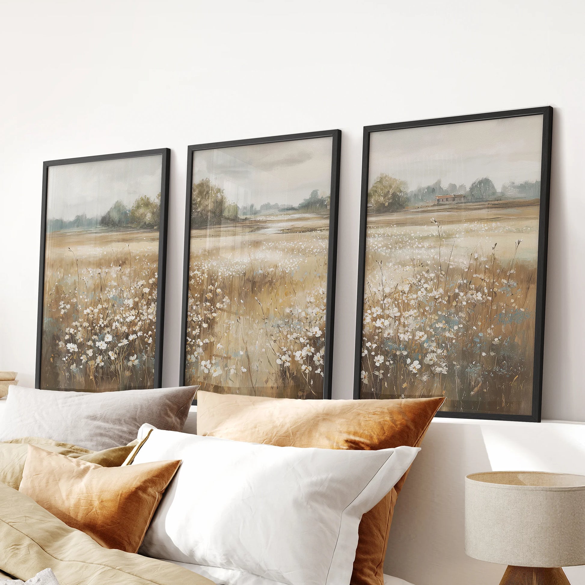 Three-piece wildflower landscape artwork in black framed prints hangs above a bedroom headboard, giving the space a soft farmhouse calm.