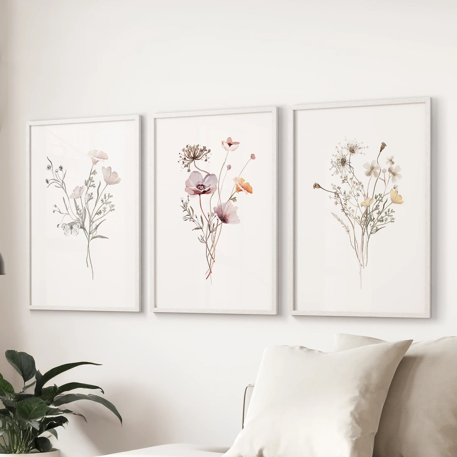 Set of three watercolor wildflower posters in white frames grounds the living room behind the couch with subtle natural texture.